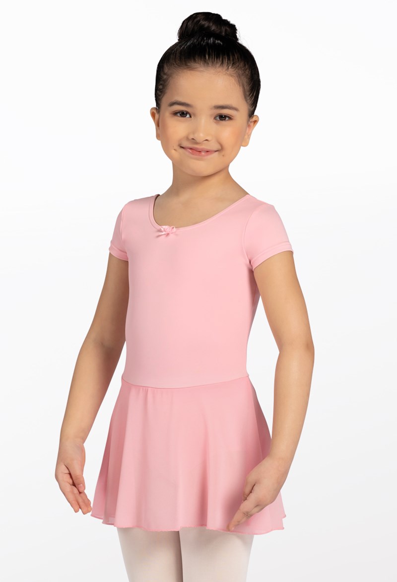A young girl with dark hair in a bun smiles and poses with arms outstretched, wearing the Pink Kids Short Sleeve Dress and white tights against a white background.