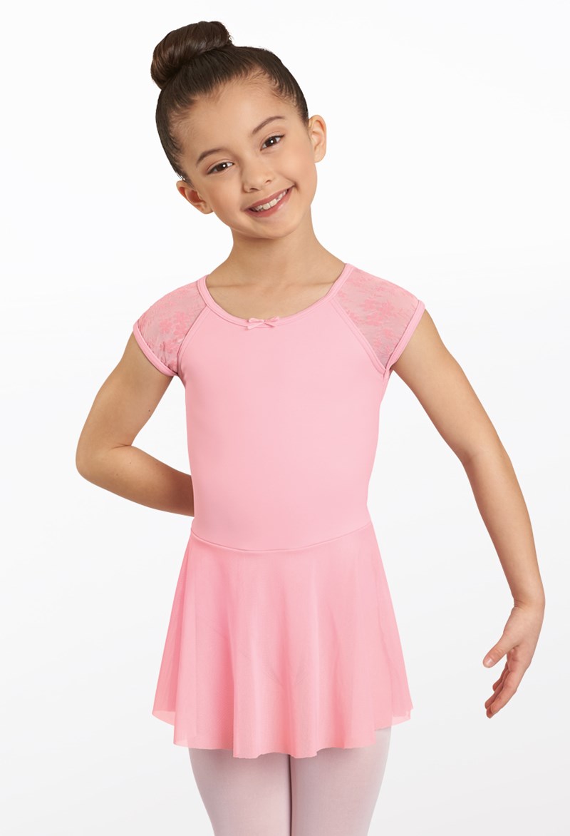 A young girl with dark hair in a bun smiles and poses with one hand on her hip, wearing the Pink Kids Floral Cap Sleeve Dress against a plain white background.