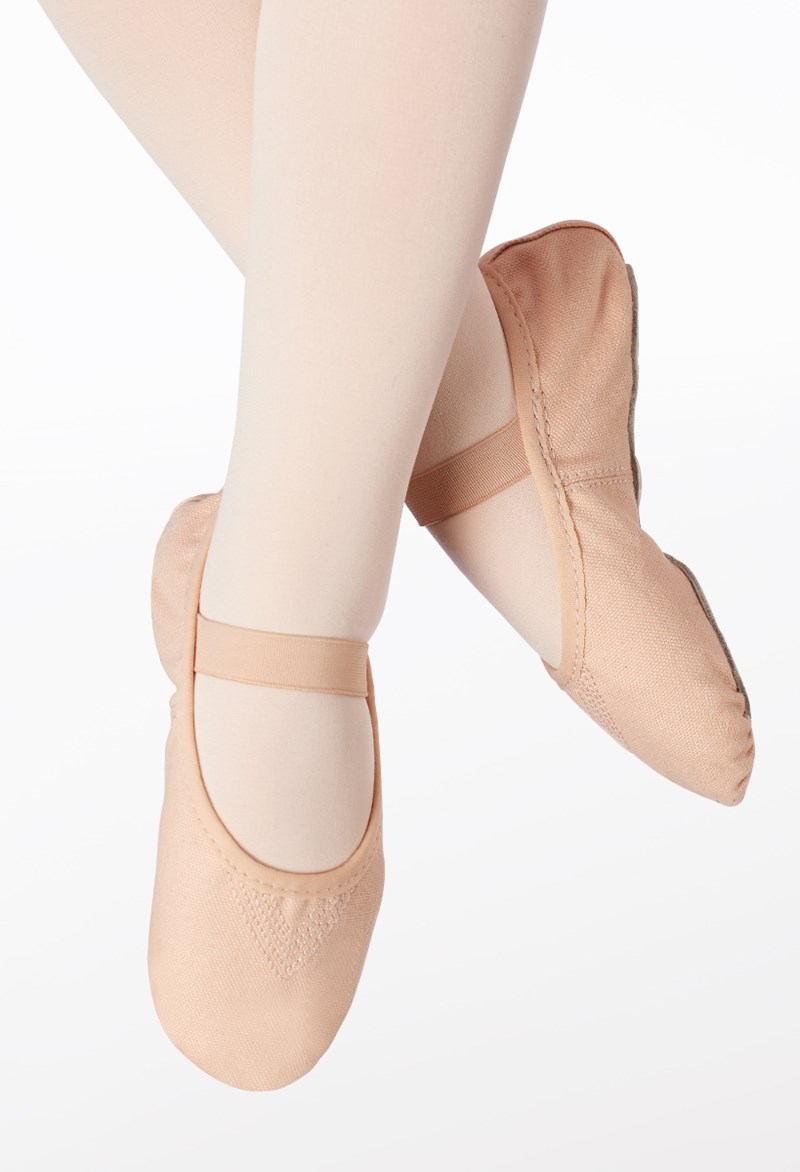 A close-up of crossed legs wearing light pink ballet tights and matching Canvas No-Tie Ballet Shoe slippers with elastic straps against a white background.