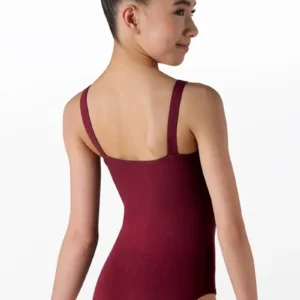 A young girl with dark hair in a neat bun models the Cotton Princess Seam Leotard in burgundy, paired with nude tights. She stands with her back to the camera, looking over her shoulder and smiling subtly.