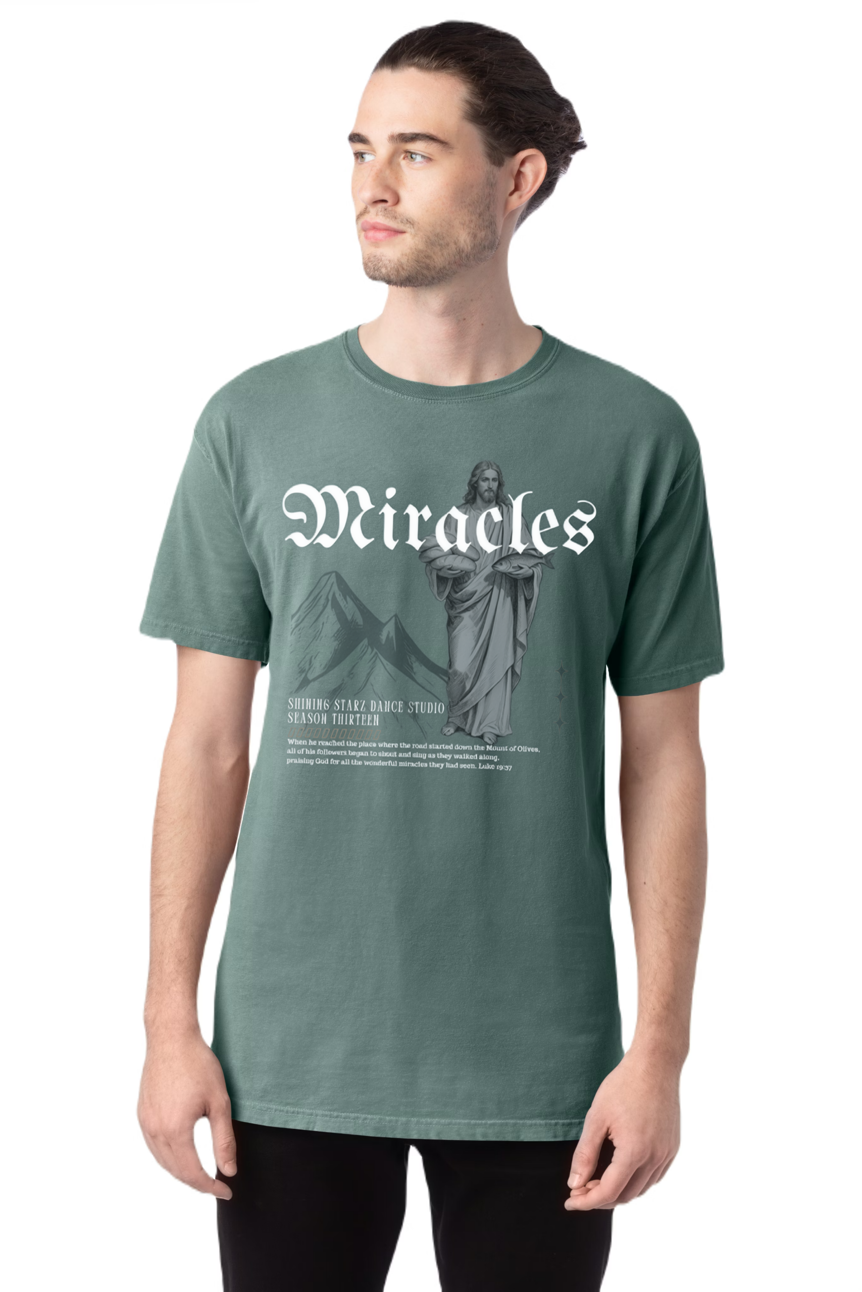 A man with long hair pulled back wears the "Miracles" T-Shirt, which features the word Miracles, an image of Jesus, mountains, and event details printed in white on the front.